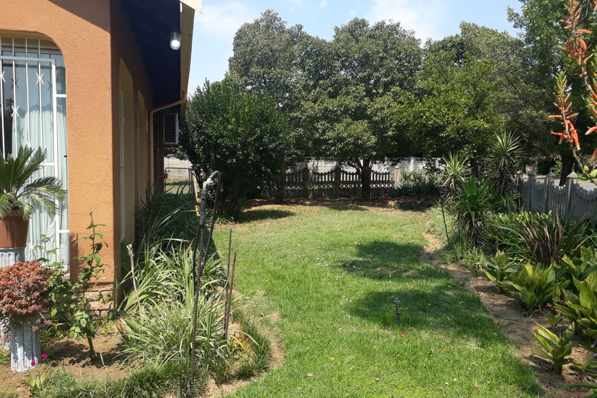 A view of the rear garden area featuring established trees, landscaped garden beds, and a side view of the house exterior with security bars.