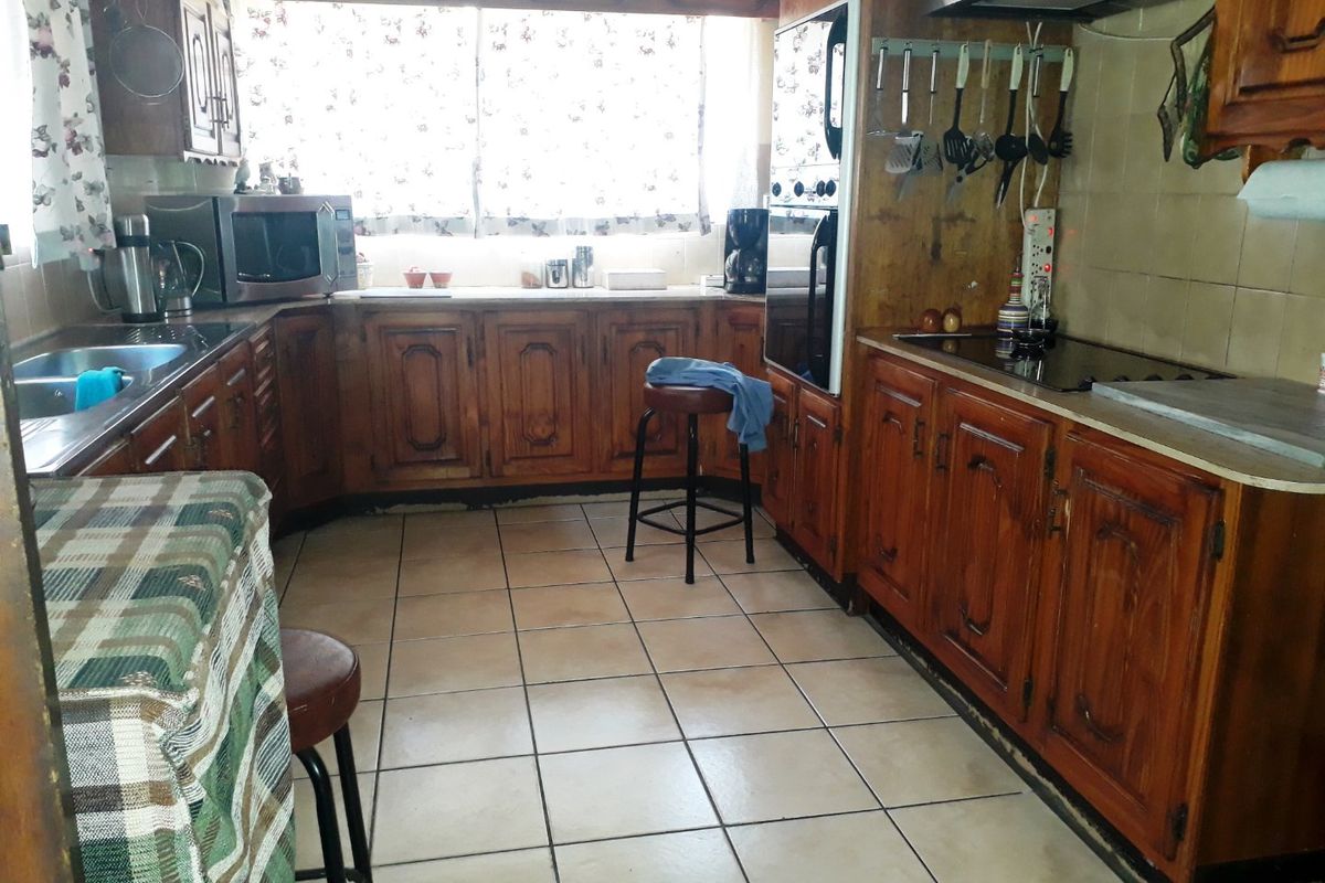 A dated kitchen featuring traditional wooden cabinetry, tiled flooring, built-in oven, and a hob, offering a functional layout with significant potential for modernization.