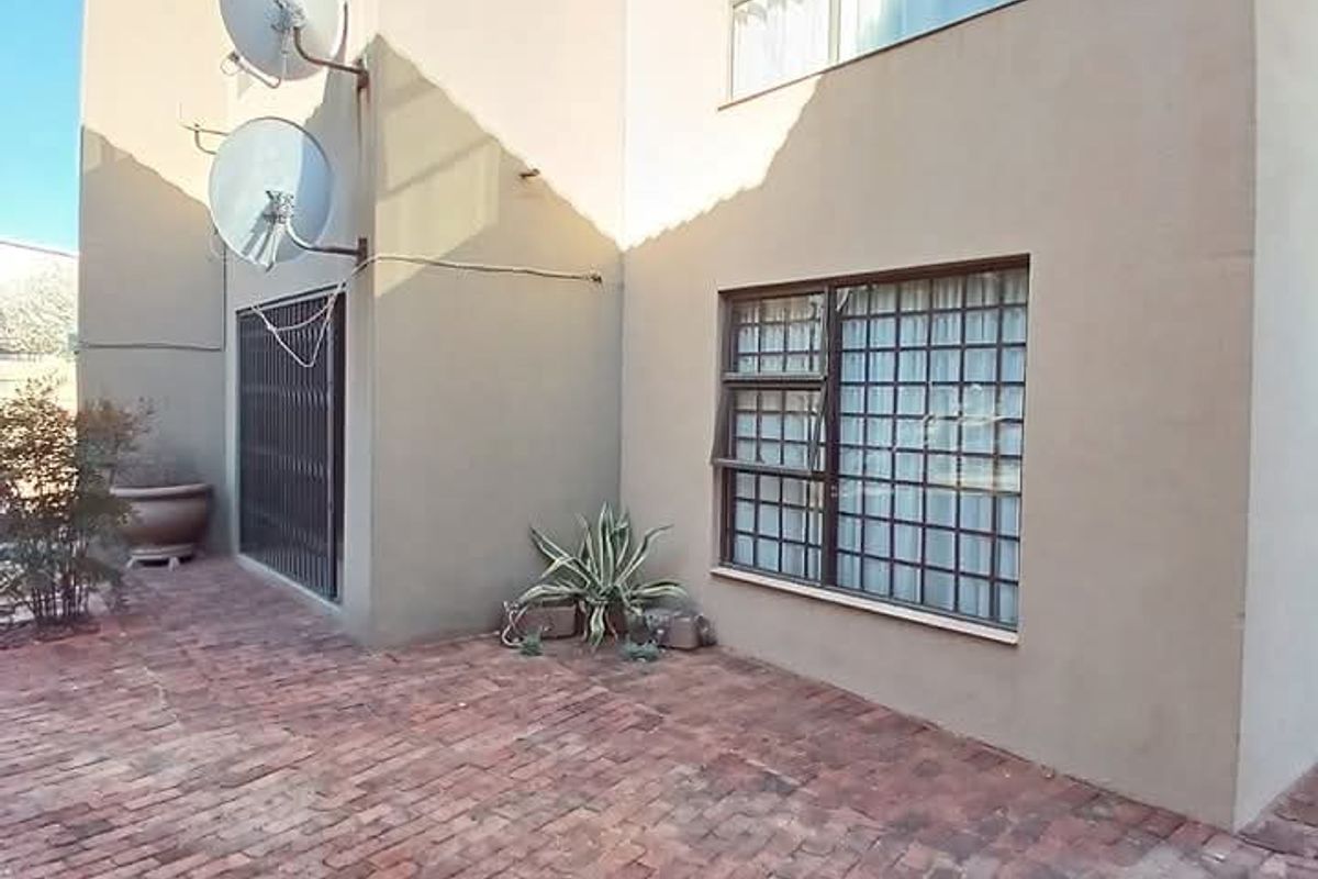 Rear exterior view of the townhouse featuring a brick-paved patio area, security bars on windows, and dual satellite dishes mounted on the wall.