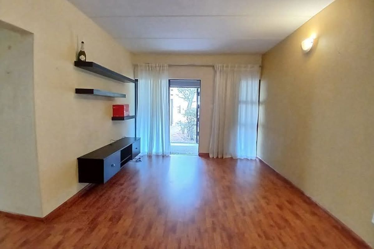 A living room featuring wood-look laminate flooring, wall-mounted shelving, and a glass door providing access to the exterior.