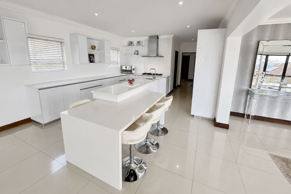 Modern, bright kitchen featuring a large central island with breakfast bar seating, sleek white cabinetry, and high-quality quartz countertops.