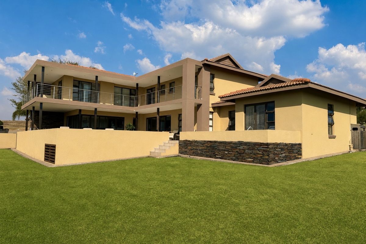 A well-maintained rear elevation of a modern double-story house featuring a spacious lawn, stone-clad retaining walls, and expansive upper-level balconies.