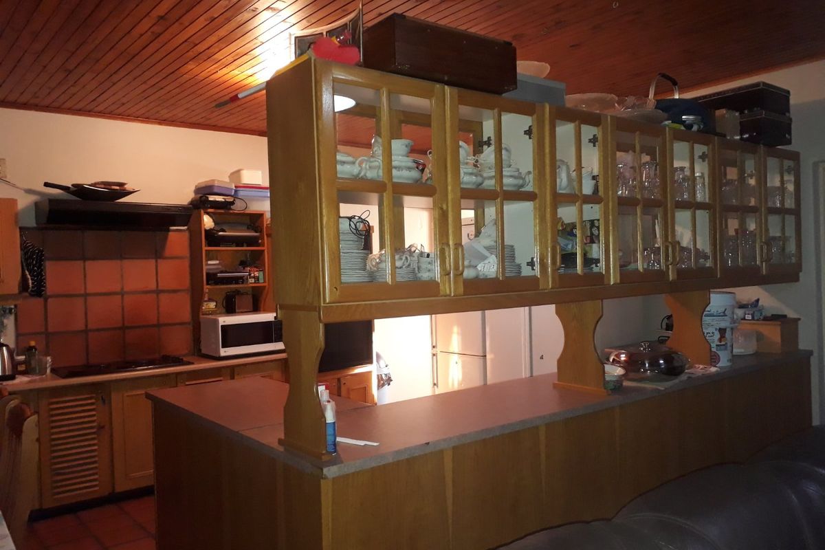 A dated kitchen featuring timber cabinetry, a breakfast bar with overhead glass-fronted display cabinets, and a timber-paneled ceiling.
