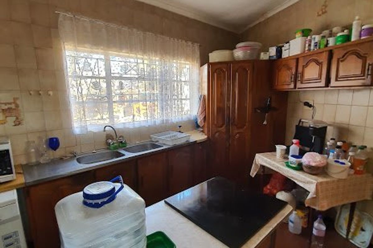 A dated kitchen featuring wooden cabinetry, tiled walls, and a double basin sink, offering a functional layout with potential for modernization.