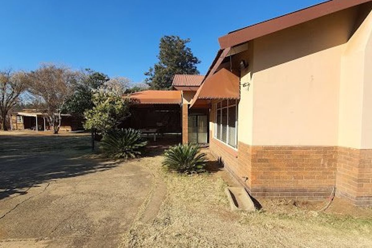 Side view of the farm property showing a brick and plaster facade, covered patio area, and surrounding grounds with a concrete driveway.