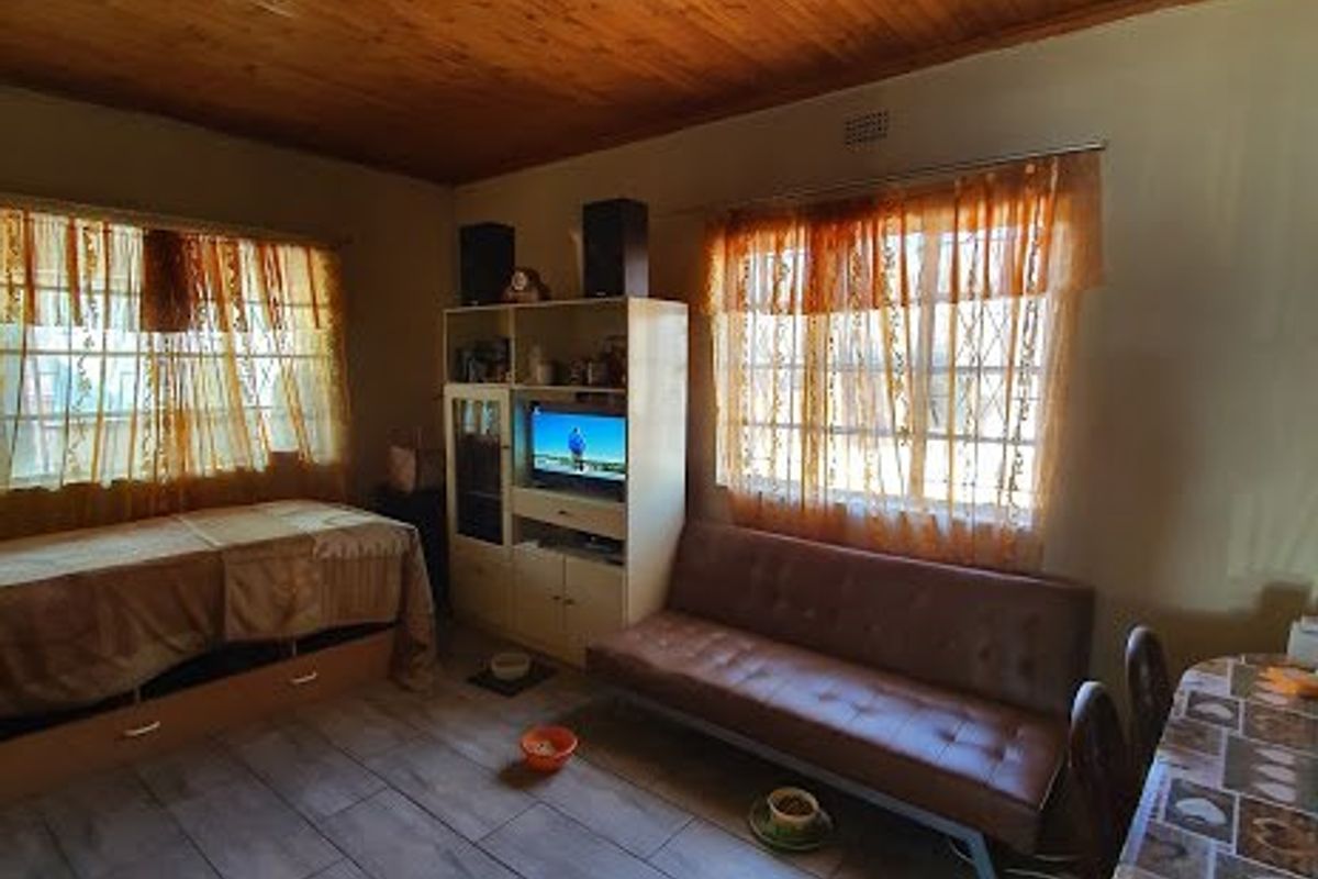 A living room featuring wood-paneled ceilings, tiled flooring, and large windows with curtains, providing a functional and lived-in space.