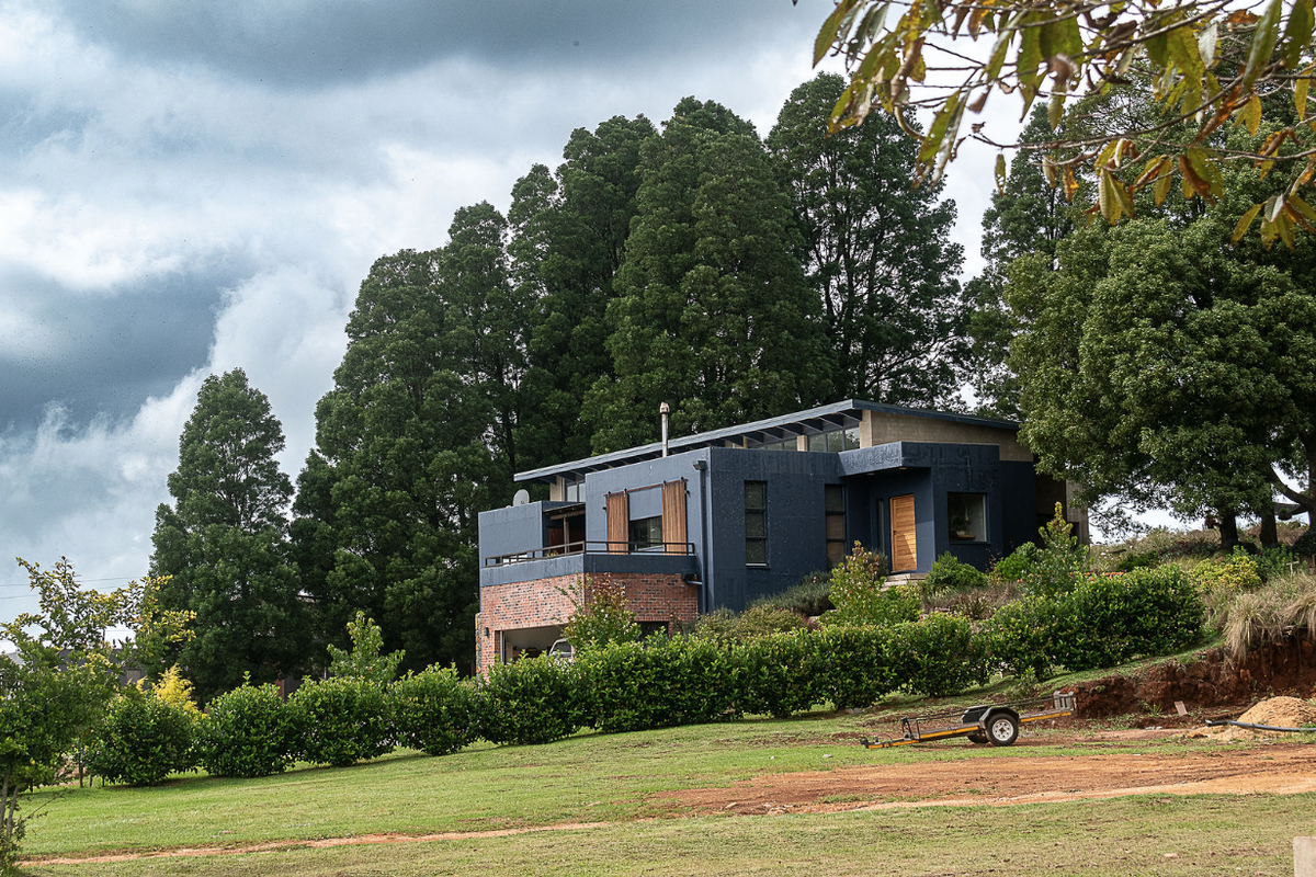 A modern multi-level home featuring a combination of brick and dark-toned cladding, set within a lush, tree-lined landscape with a spacious balcony.