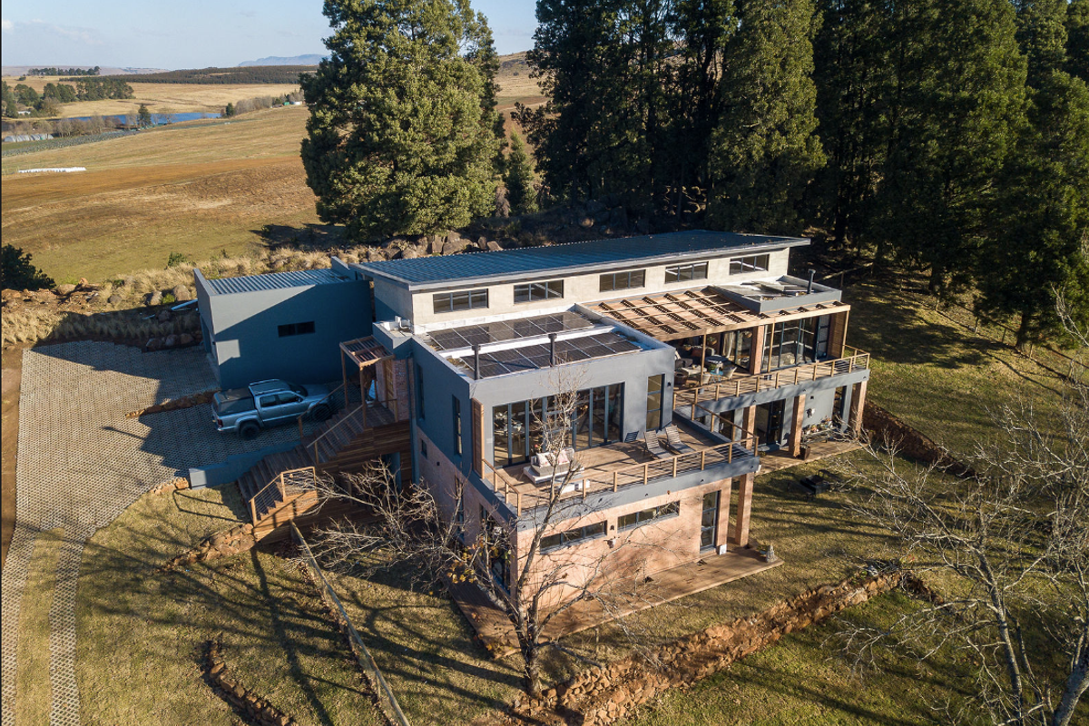 Aerial view of a modern multi-level home featuring solar panels, extensive timber decking, and large windows set in a rural landscape.