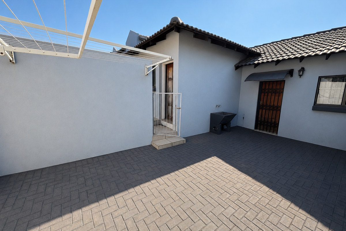 A clean and well-maintained rear courtyard featuring paved flooring, a wall-mounted washing line, a utility sink, and secure access points.