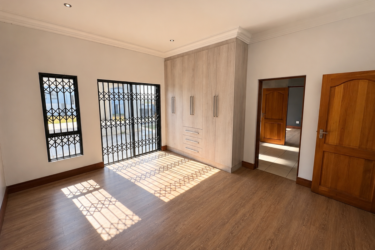 Spacious bedroom featuring light wood-finish built-in cupboards, durable laminate flooring, and secure metal gates on the windows and sliding door.