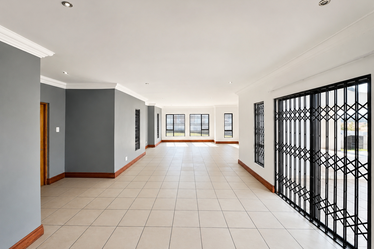 A spacious, empty living area featuring neutral tiled flooring, recessed lighting, and secure metal gates leading to the exterior.