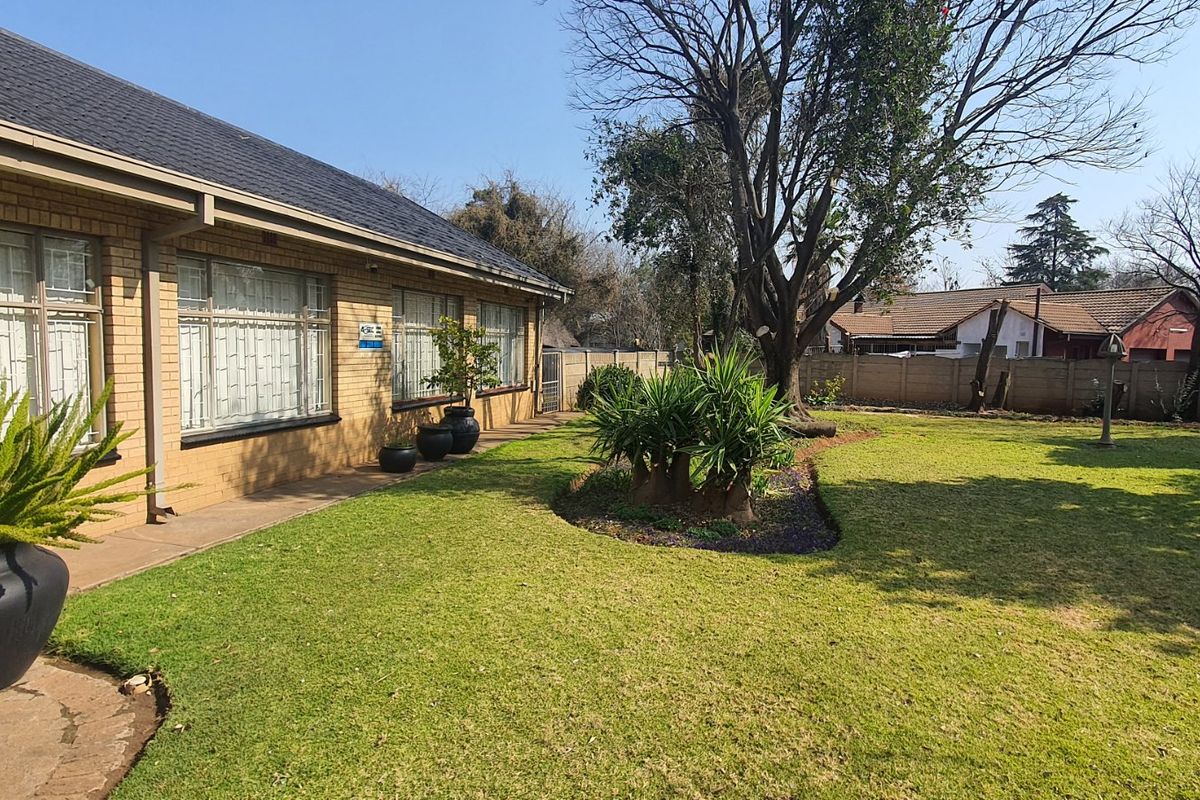 A view of the rear garden featuring a well-maintained lawn, mature trees, and the rear brick facade of the house.