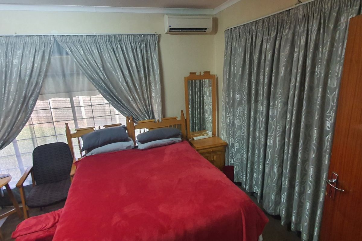 A bedroom featuring a wall-mounted air conditioning unit, large windows with curtains, and a wooden door.
