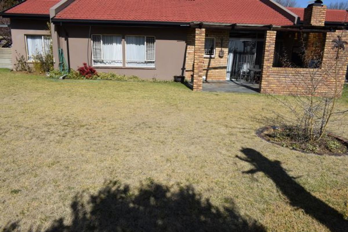 Rear view of the house featuring a covered brick patio, red tiled roof, and a spacious garden area.