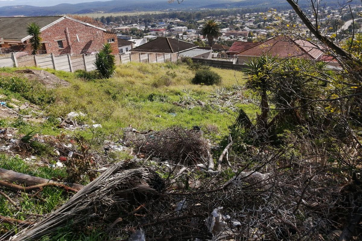 A sloped vacant residential plot featuring natural vegetation and panoramic views of the surrounding neighborhood and distant mountains.