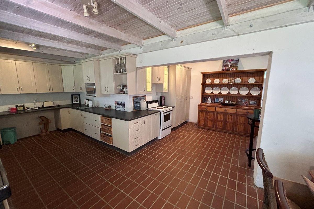 Spacious kitchen featuring light-toned cabinetry, dark countertops, a freestanding stove, and a distinctive exposed timber beam ceiling with terracotta-style tiled flooring.