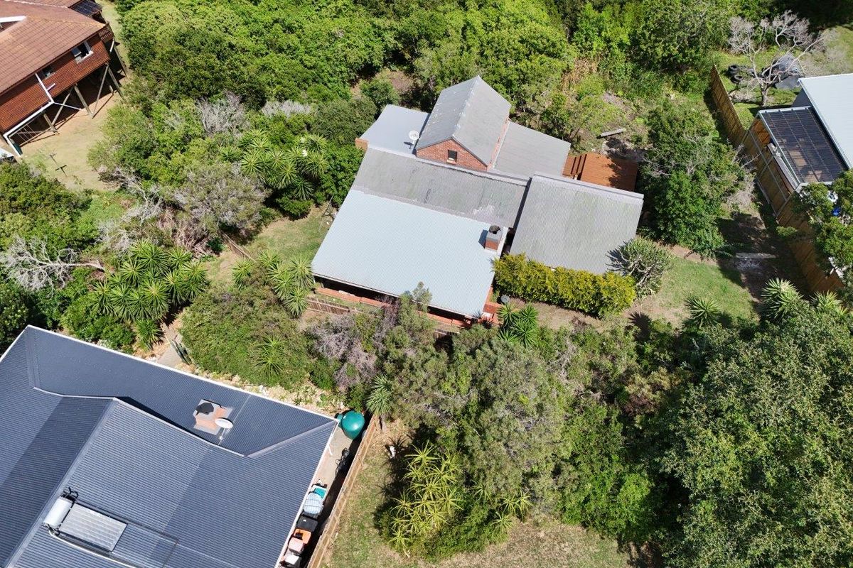 Aerial view of a residential property featuring a multi-pitched metal roof, surrounded by established trees and garden areas.