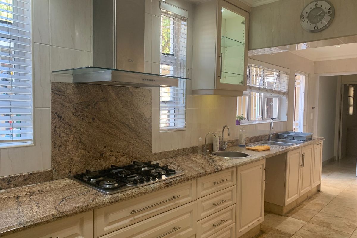 A well-appointed kitchen featuring granite countertops, a built-in gas hob, stainless steel extractor fan, double sink, and classic cabinetry with glass-front display units.