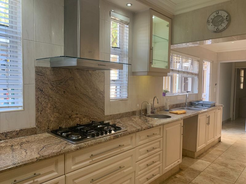 A well-appointed kitchen featuring granite countertops, a built-in gas hob, stainless steel extractor fan, double sink, and classic cabinetry with glass-front display units.