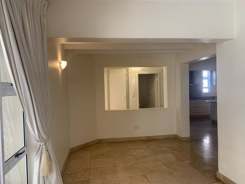 An open-plan living area featuring neutral floor tiles, exposed ceiling beams, and a serving hatch connecting to the kitchen space.