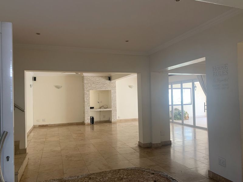 Spacious open-plan living area featuring tiled flooring, a stone-clad feature wall with built-in shelving, and large sliding doors leading to an outdoor patio.
