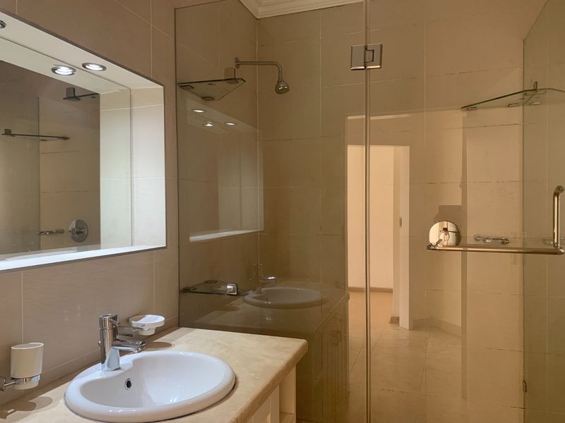 Modern bathroom featuring a glass-enclosed shower, stone-topped vanity with integrated basin, and a large wall-mounted mirror with recessed lighting.