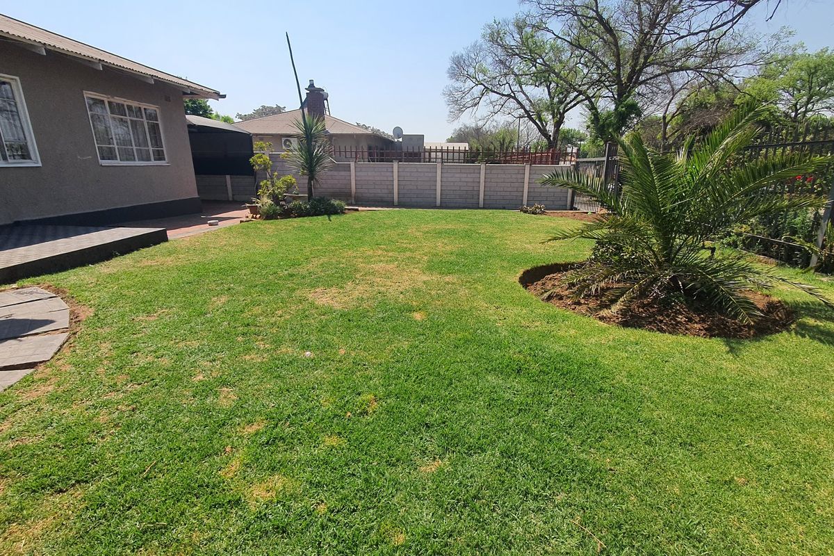 A spacious rear garden featuring a well-maintained lawn, paved walkway, and perimeter boundary wall, providing a private outdoor space for the property.