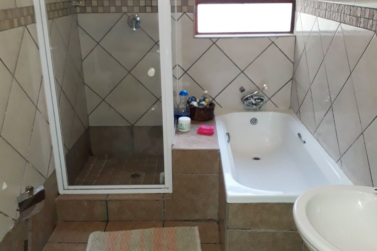 A functional bathroom featuring a separate shower enclosure, a built-in bathtub, and a pedestal basin with tiled walls and flooring.