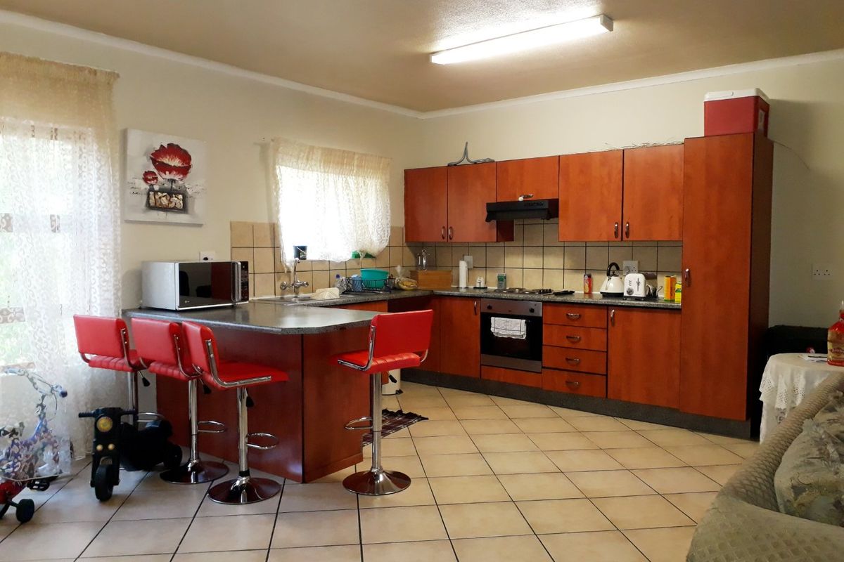 A functional kitchen featuring wood-look cabinetry, a breakfast bar, built-in oven, hob, and extractor fan with tiled flooring throughout.
