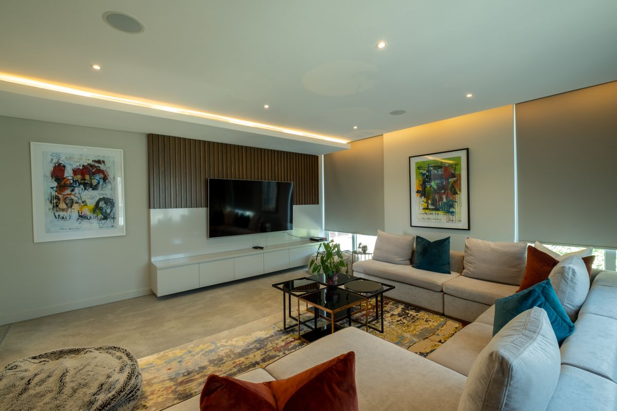 Modern living room featuring a custom built-in media console, timber slat feature wall, recessed LED strip lighting, and integrated ceiling speakers.