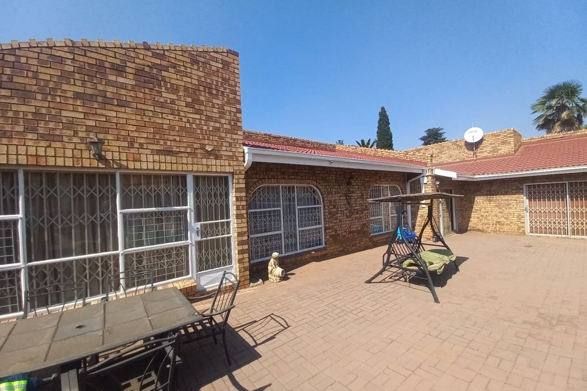 A spacious rear patio area featuring face brick exterior walls, paved flooring, and secure metal window and door grilles.