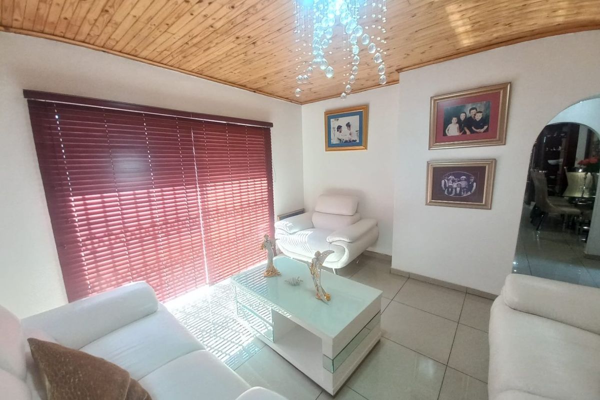 A living room featuring tiled flooring, a timber tongue and groove ceiling, and a decorative crystal chandelier, providing a warm and inviting atmosphere.