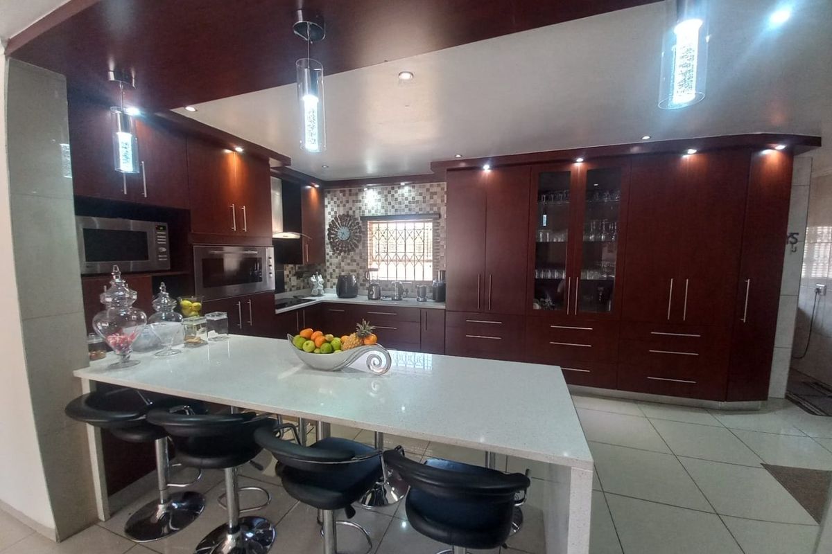 Modern kitchen featuring dark wood cabinetry, a large stone-topped island, built-in appliances, mosaic tile backsplash, and contemporary pendant lighting.
