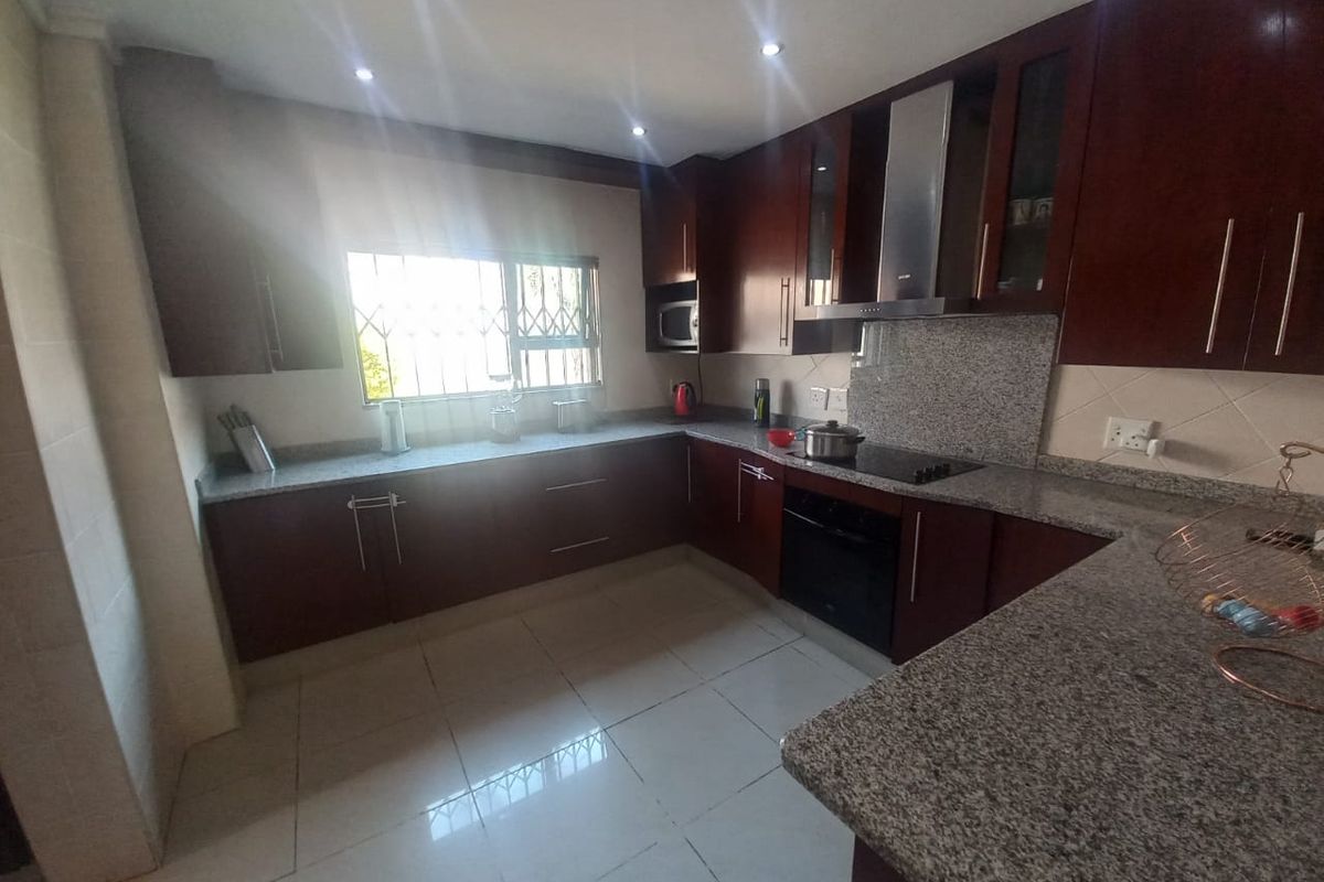 A functional kitchen featuring dark wood cabinetry, granite countertops, a built-in oven, hob, and extractor fan with tiled flooring.