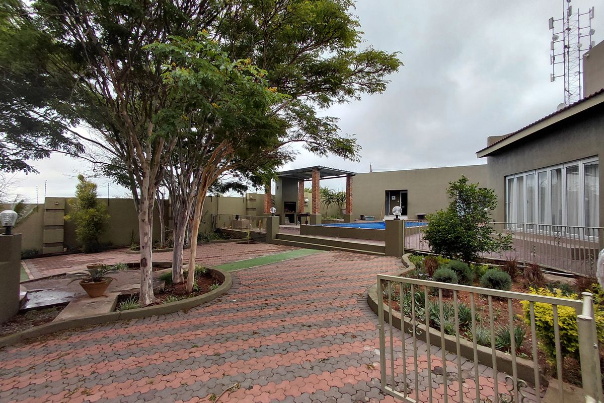 Spacious rear garden featuring a paved courtyard, swimming pool, and a covered outdoor entertainment area with a built-in braai.