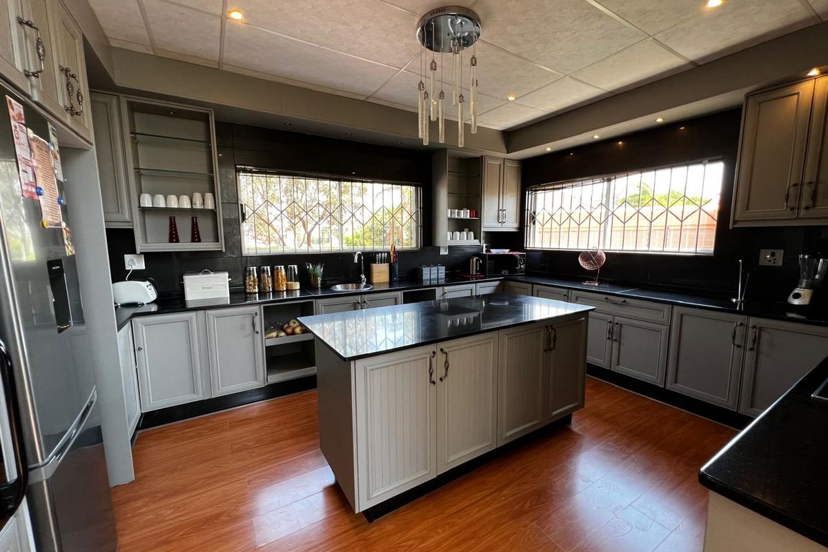 A spacious kitchen featuring grey cabinetry, dark countertops, a central island, and wood-look flooring, complemented by recessed lighting and security bars on windows.