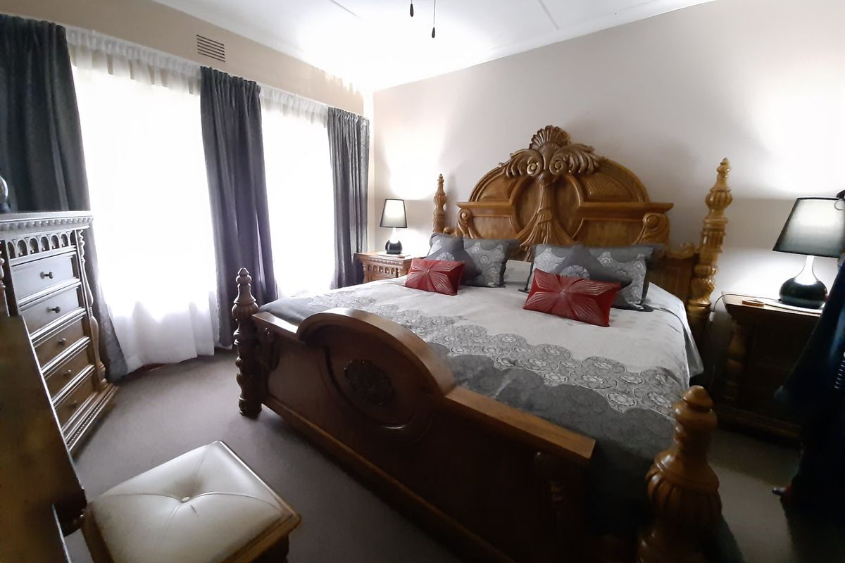 A spacious bedroom featuring neutral wall tones, carpeted flooring, and large windows with curtains, providing a comfortable and functional living space.