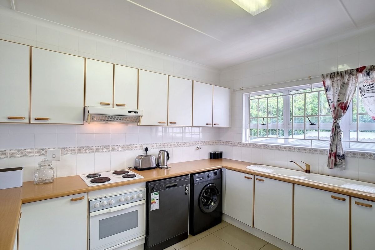 A functional kitchen featuring white cabinetry, laminate countertops, a built-in oven with hob, extractor fan, and integrated space for laundry and dishwashing appliances.