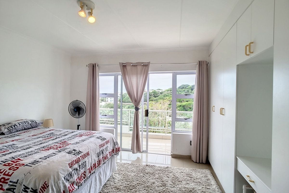 Bright bedroom featuring built-in wardrobes, tiled flooring, and sliding glass doors opening onto a private balcony with scenic views.