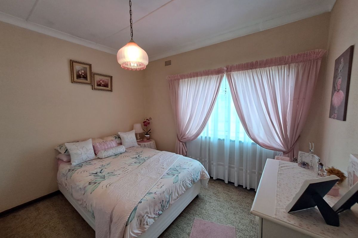 A cozy bedroom featuring neutral wall tones, carpeted flooring, and a large window dressed with curtains, providing a comfortable and functional living space.