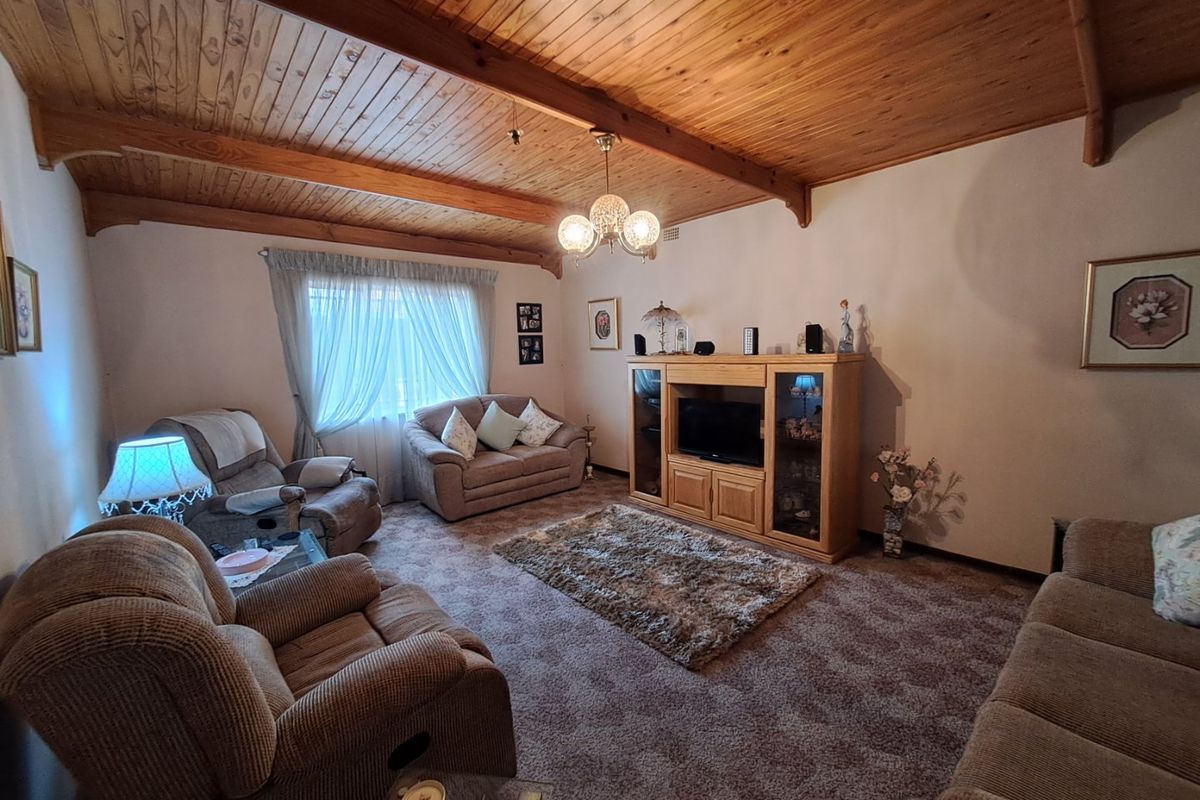 A cozy living room featuring a vaulted timber-paneled ceiling with exposed beams and carpeted flooring.