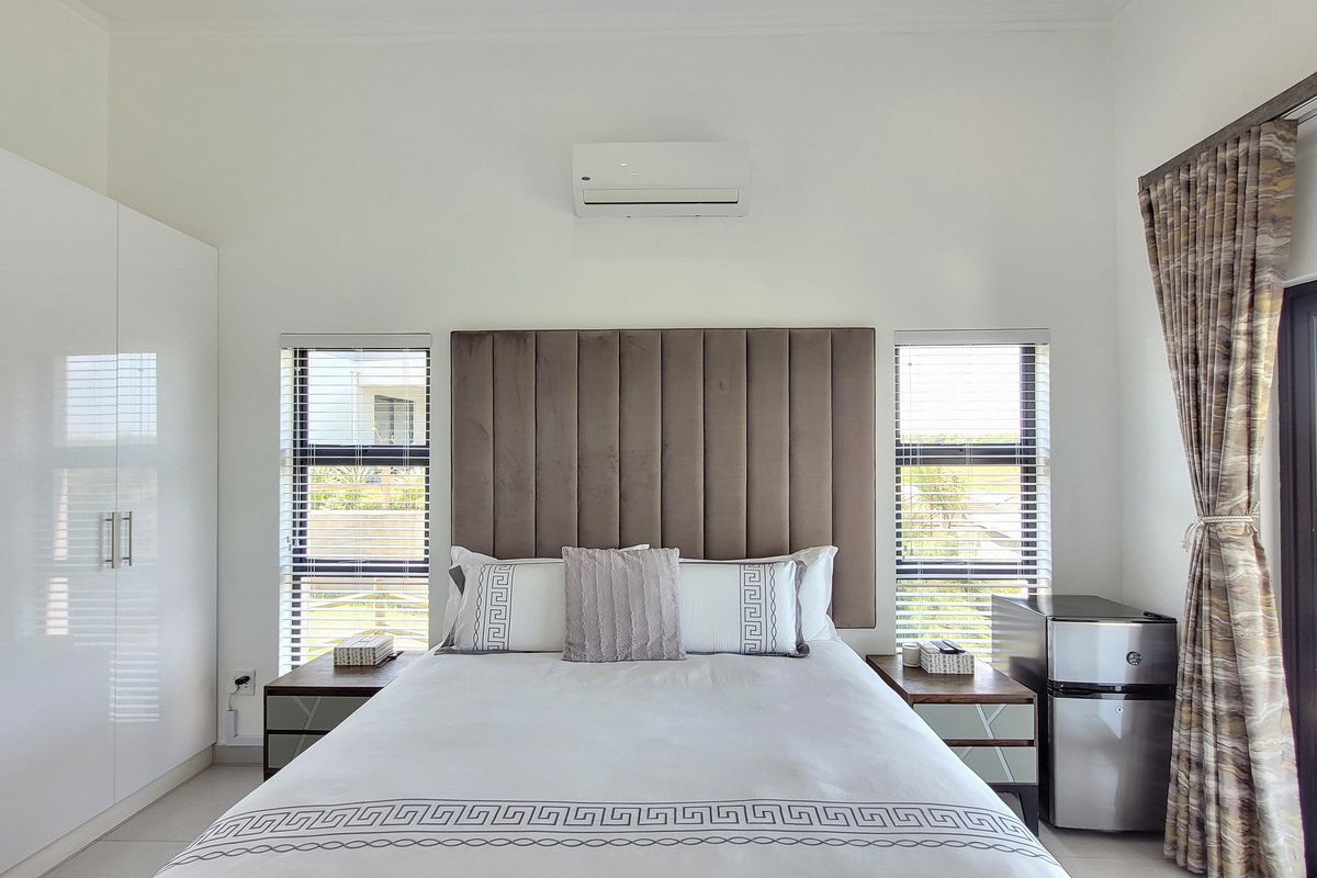 A well-maintained bedroom featuring built-in wardrobes, a wall-mounted air conditioning unit, and large windows with fitted blinds.