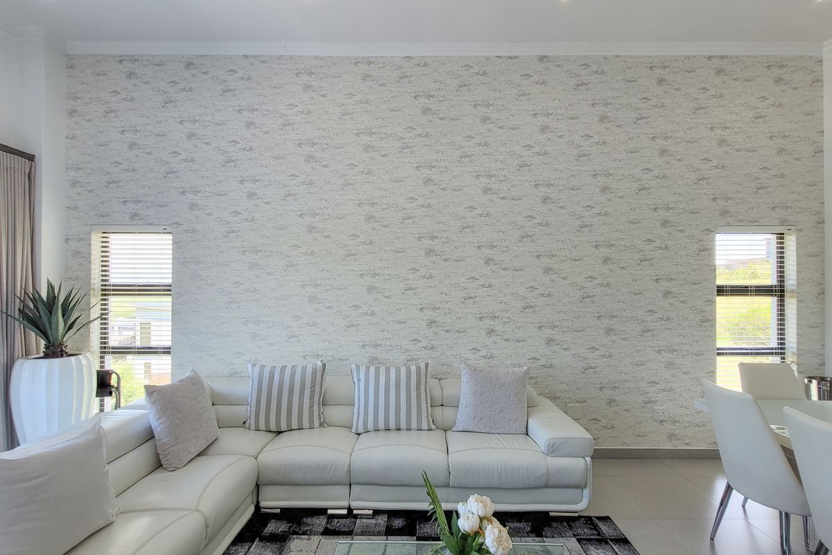 A bright and spacious living area featuring a large feature wall with textured wallpaper and dual vertical windows providing natural light.
