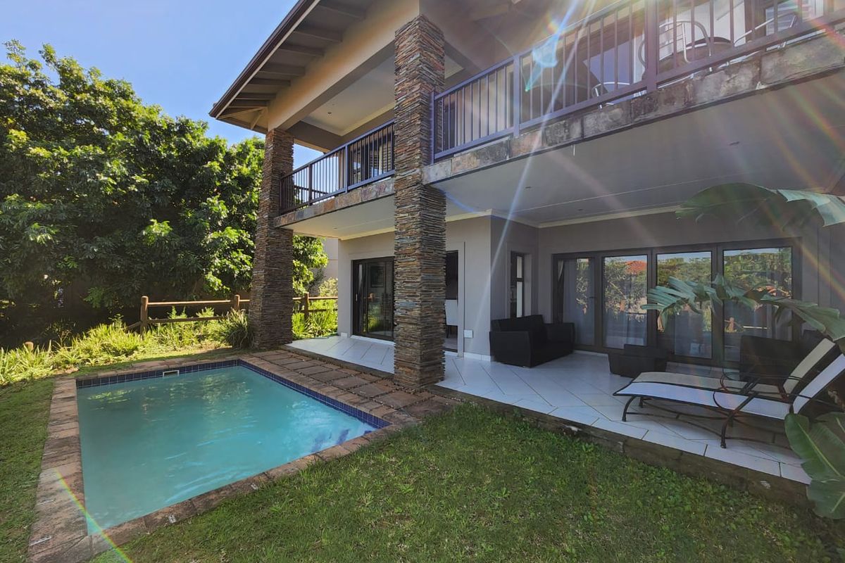 A spacious rear patio area featuring a swimming pool, stone-clad support pillars, and a covered balcony overlooking the garden.