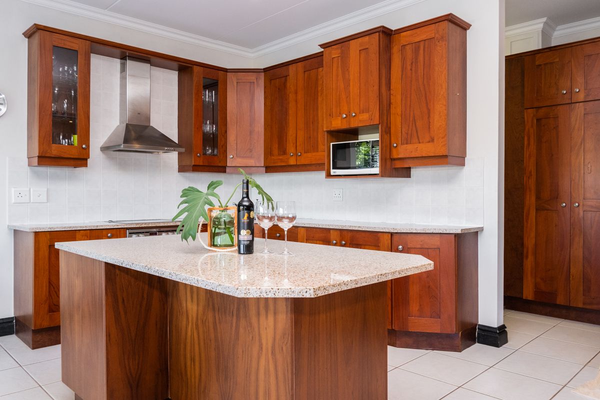 A well-maintained kitchen featuring warm-toned wooden cabinetry, granite countertops, a central island, and stainless steel extractor fan.