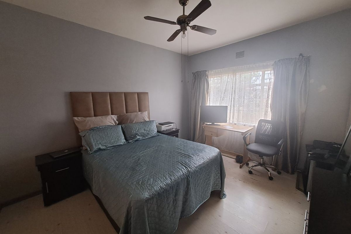 A bedroom featuring a ceiling fan, light-toned flooring, and a window with curtains, providing a functional and comfortable living space.