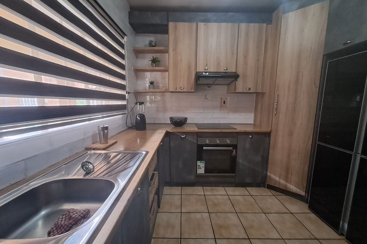 Modern kitchen featuring wood-look cabinetry, integrated oven and hob, stainless steel double sink, and tiled flooring with ample storage space.