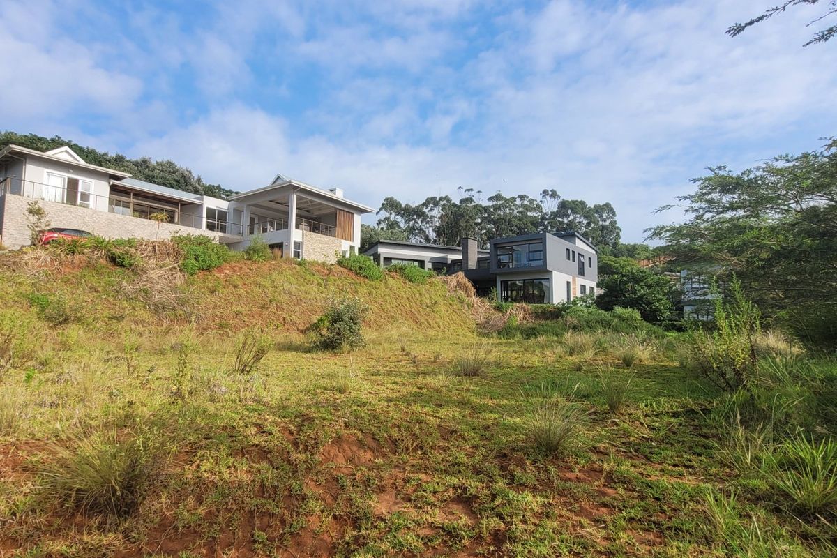 A view of the vacant residential land featuring a sloped terrain with native vegetation, overlooking neighboring modern multi-story residential properties.