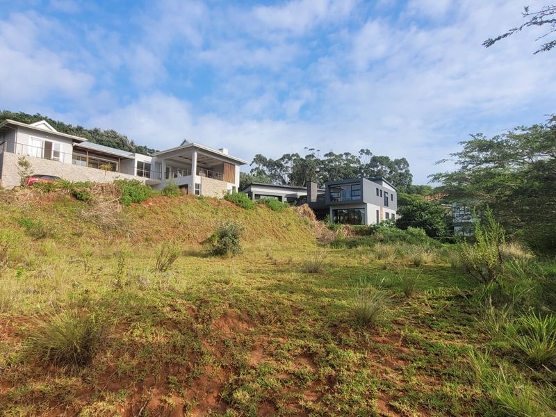 A view of the vacant residential land featuring a sloped terrain with native vegetation, overlooking neighboring modern multi-story residential properties.