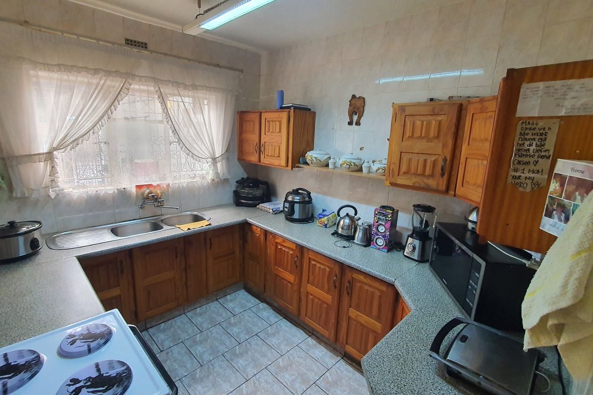 A functional kitchen featuring wooden cabinetry, laminate countertops, a double-basin sink, and tiled flooring, offering a traditional layout with ample storage space.